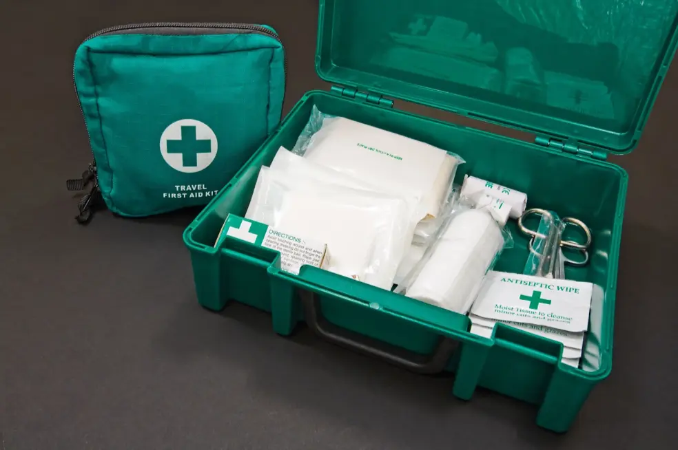 A green first aid box filled with medical supplies positioned next to a smaller travel first aid kit.