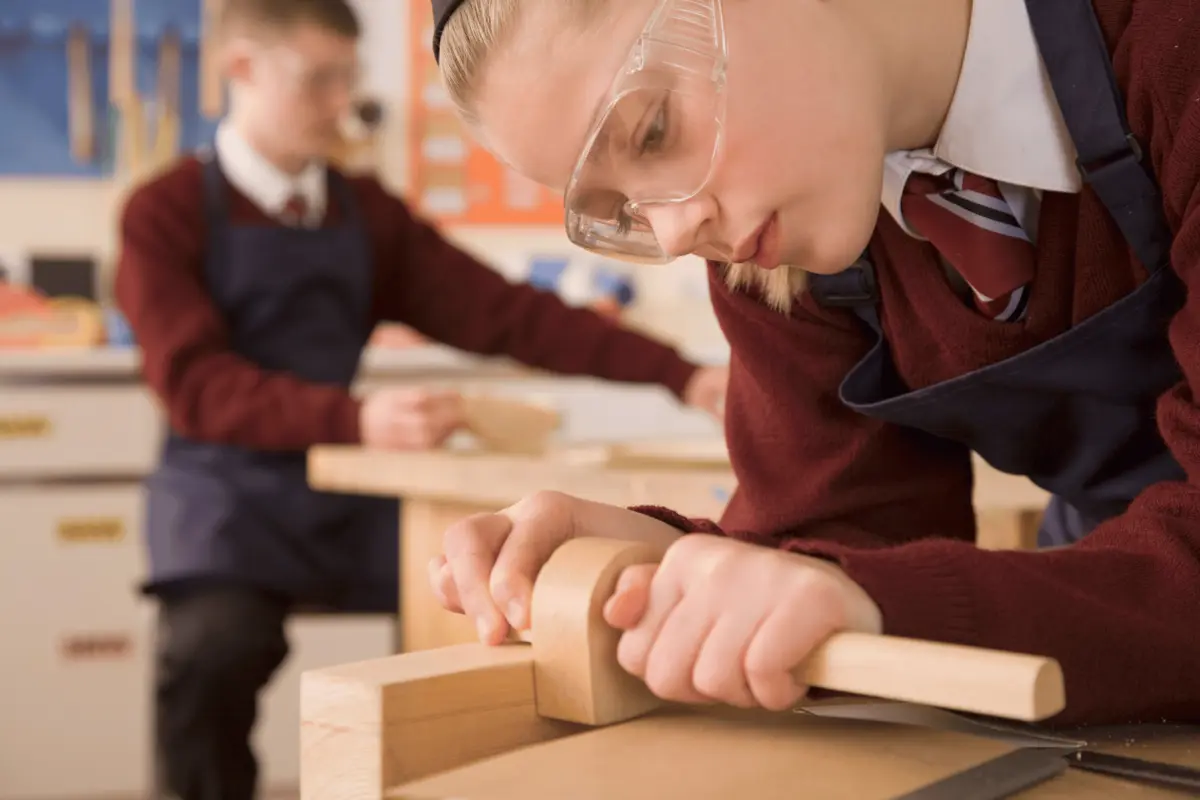Secondary school student wearing protective goggles makes wooden guitar in a design and technology class